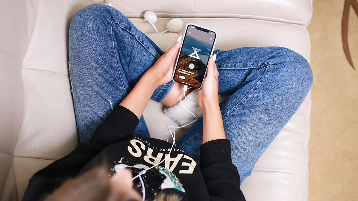 Woman sitting on couch listening to guided meditation with phone in lap