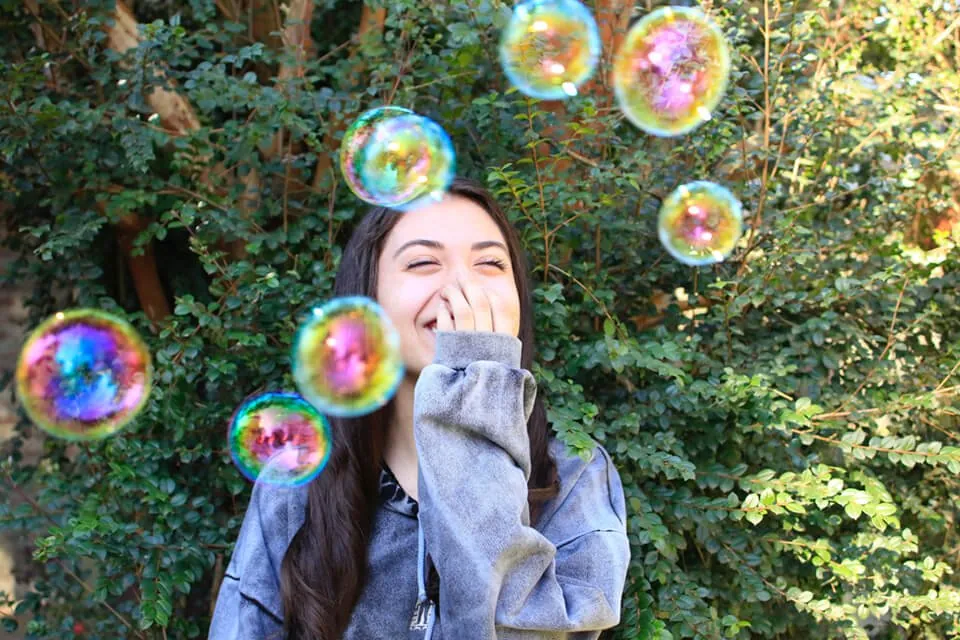 Woman covering her mouth laughing with bubbles floating around her