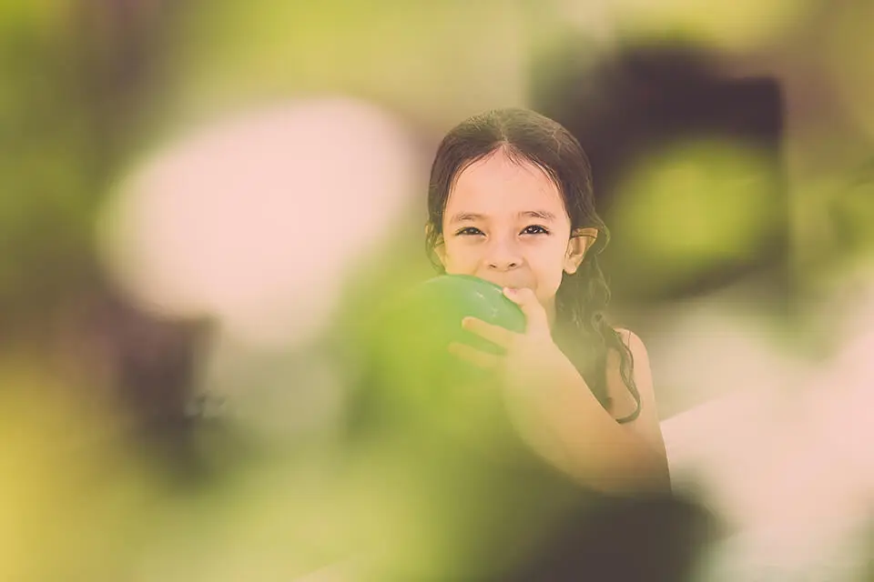 Smiling little girl blowing up green balloon