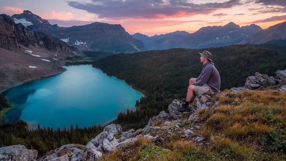 Man sitting on ridge, peacefully overlooking a still lake.