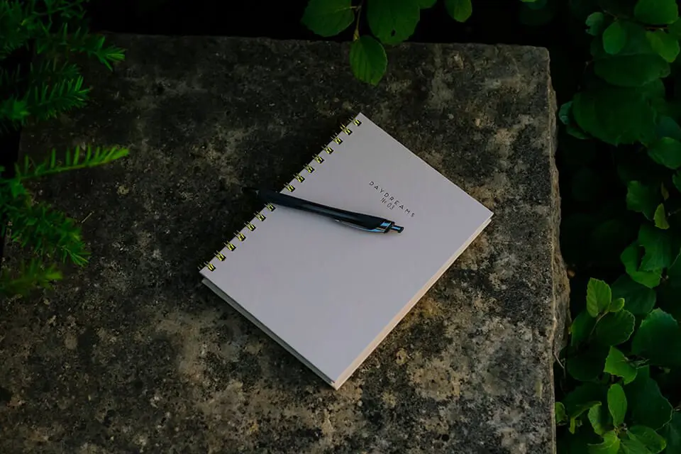 Journal with pen laying on a stone bench outdoors