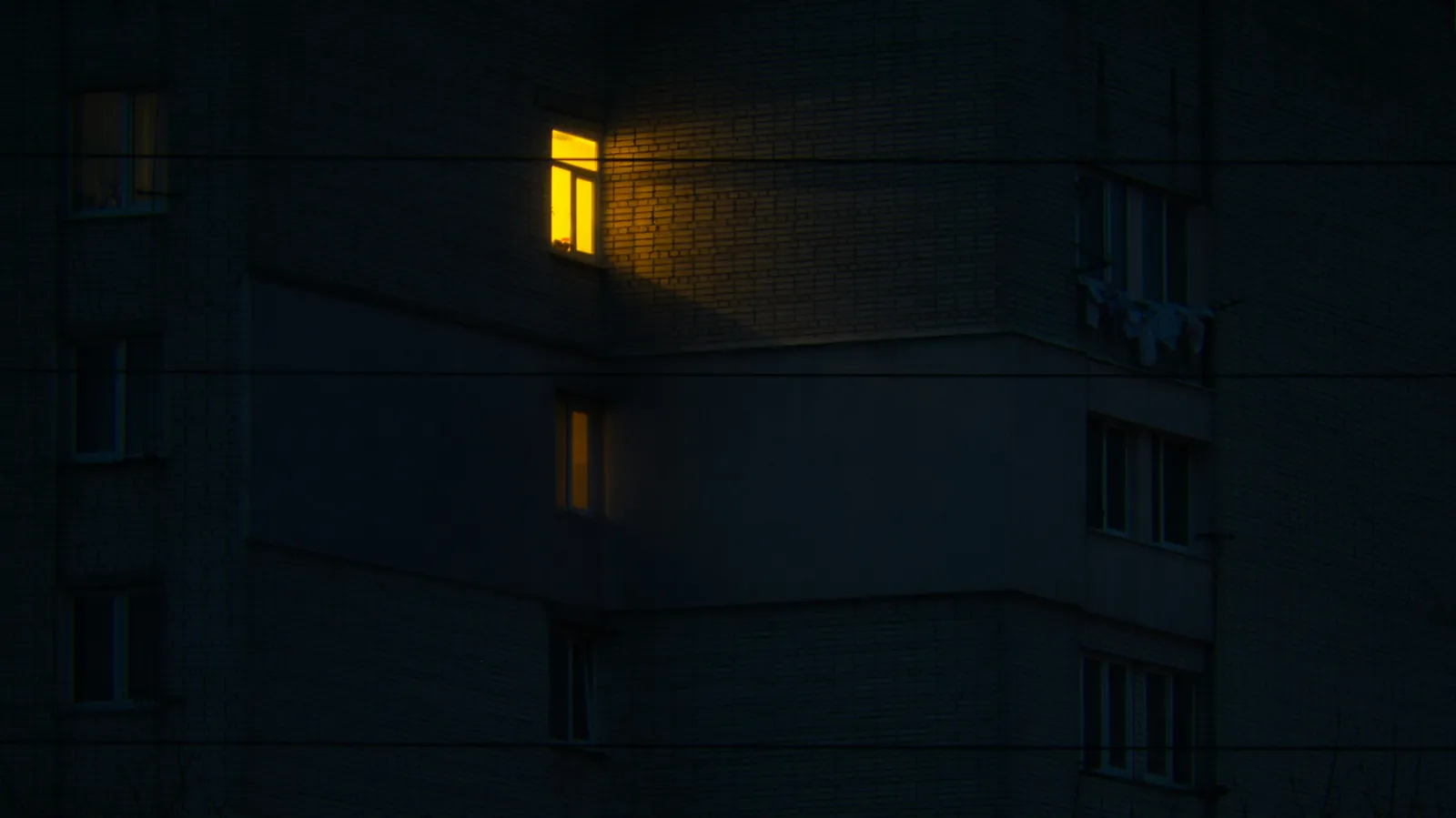 A single window lit at night against a dark apartment building facade.