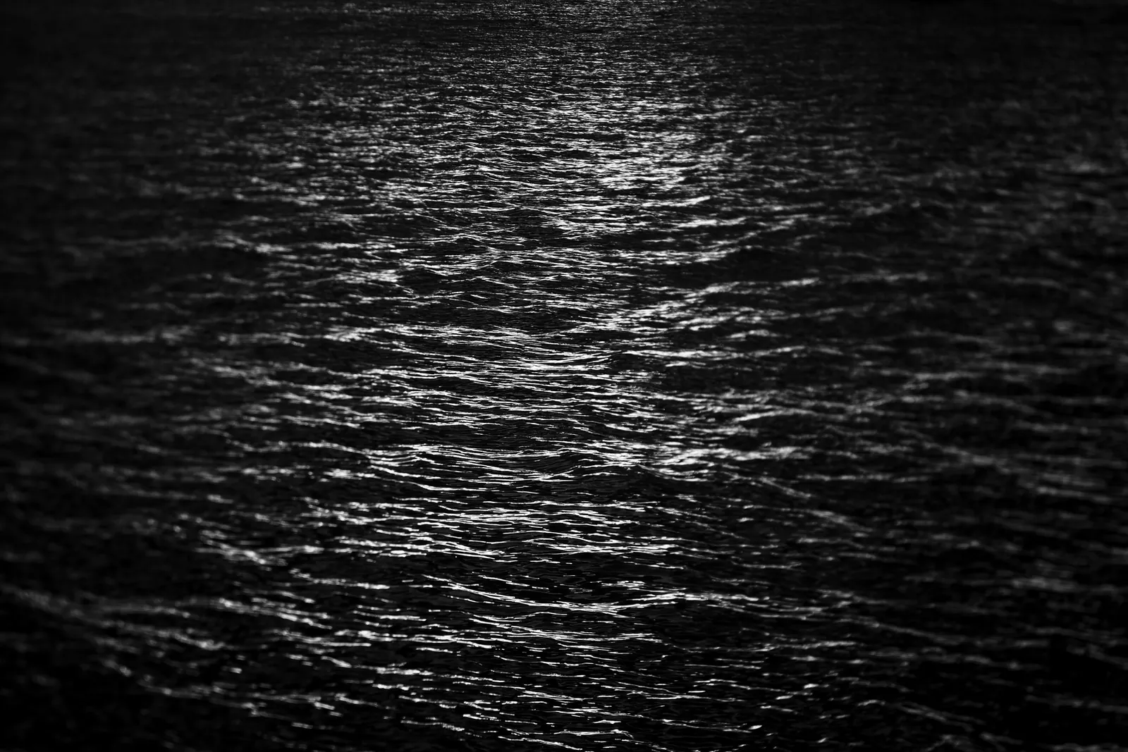 Moonlight on calm dark water with soft ripples in deep blue.