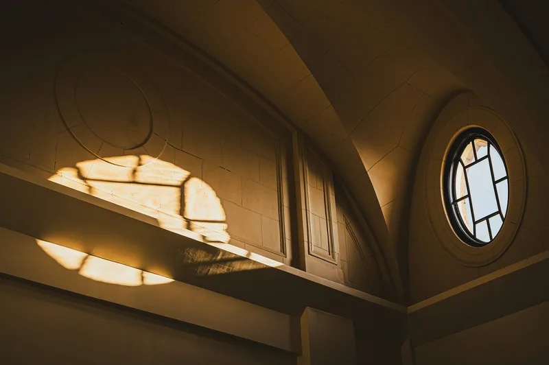 Warm golden light breaking through a round window onto a pale wall