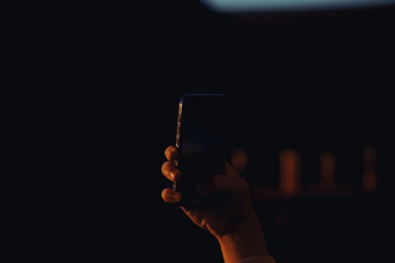 A hand holding a glowing smartphone in a darkened room
