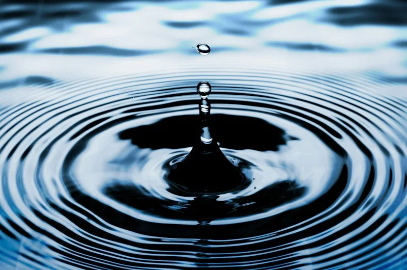 A single raindrop spreading rings across still water, suggesting one small thought rippling outward