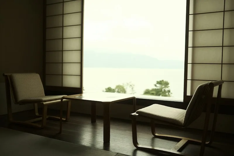 A quiet room with two simple chairs by a window and soft light over a calm view