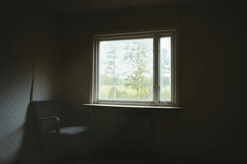 Soft daylight falling across a plain room, a chair by the window