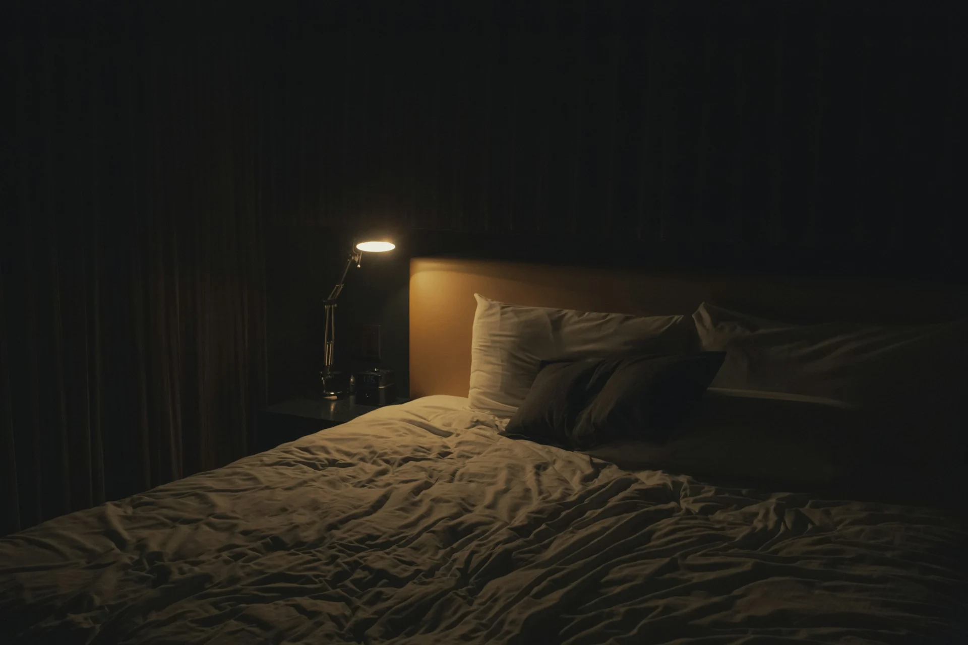 A dark, calm bedroom at night lit softly by a single warm lamp