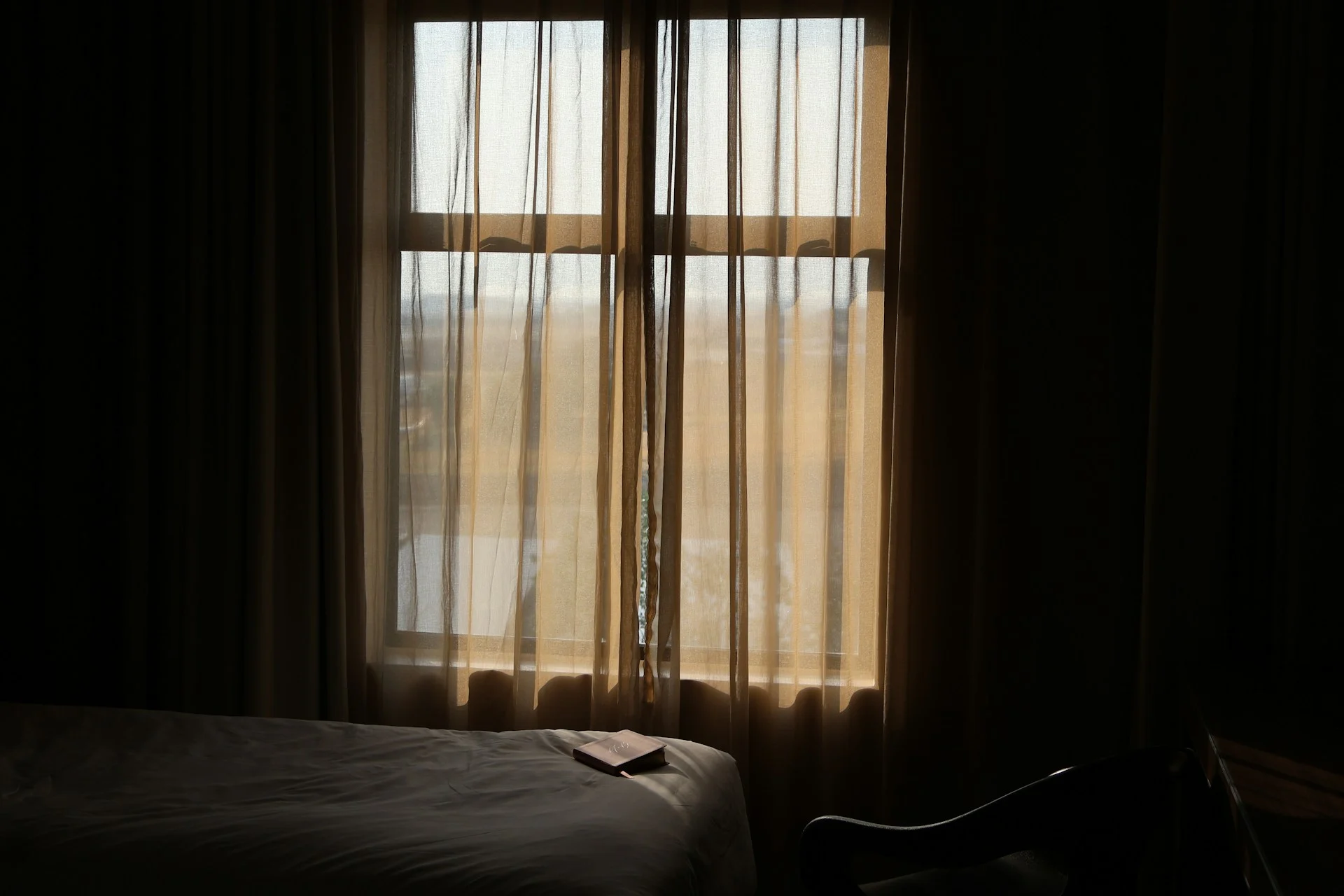 Pale early-morning light coming through sheer curtains into a still, quiet bedroom.