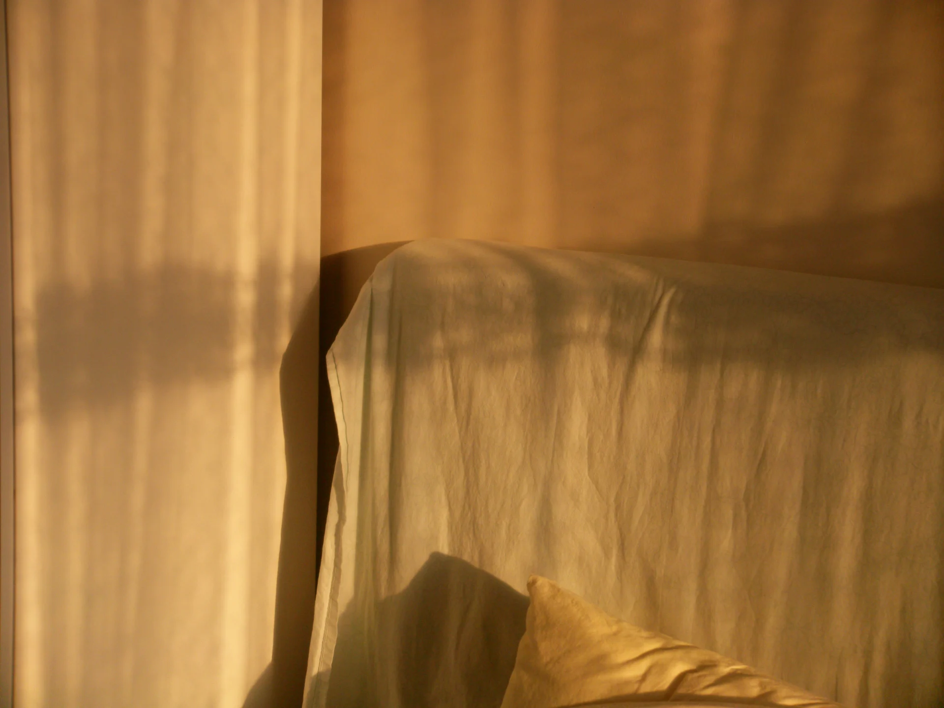 Warm light and soft shadows falling across a bed and sheer curtain in a calm, quiet room.