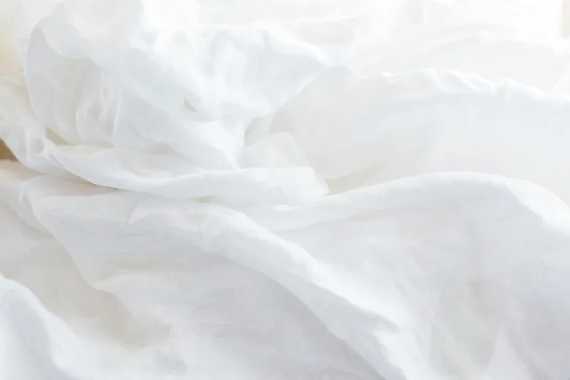 Soft, rumpled white bed linens in bright, gentle daylight.