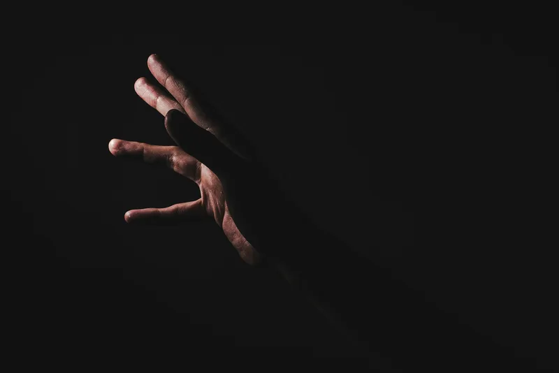 A tensed hand emerging from shadow, fingers drawn tight.