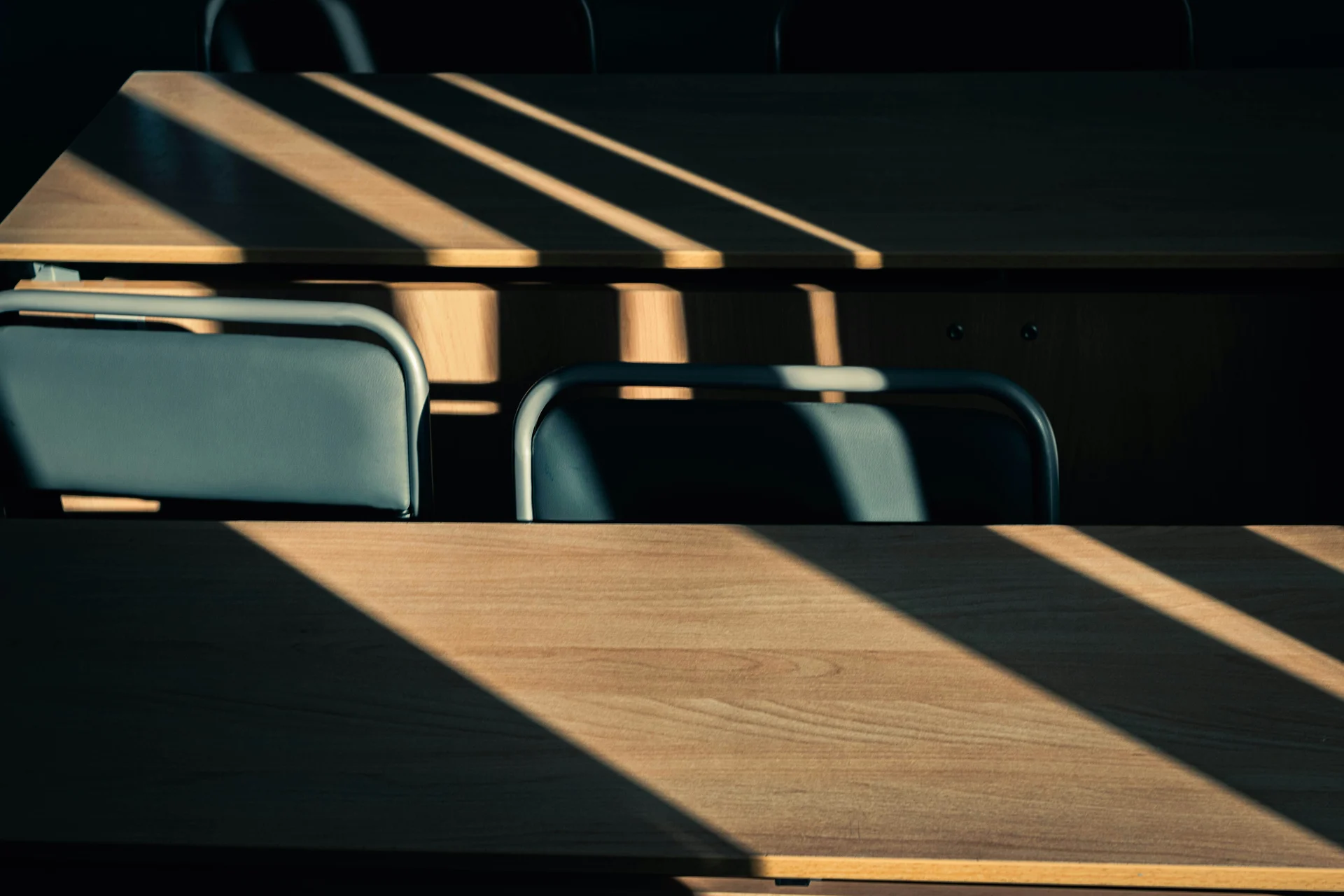 Sunlight streaming through window blinds onto an empty wooden desk in a quiet home office