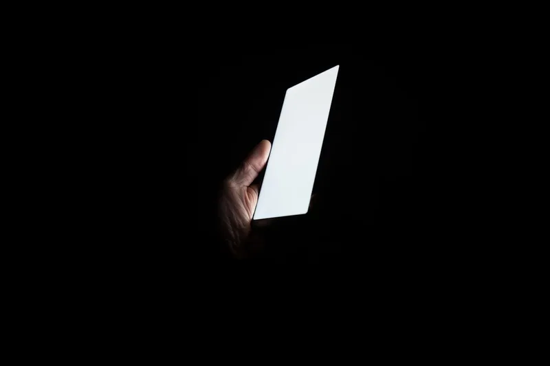 A hand holding a glowing phone screen in an otherwise dark room at night.
