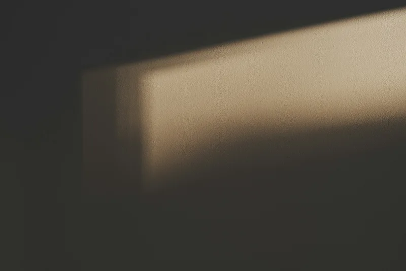 A dim wall with a soft band of warm light emerging from shadow