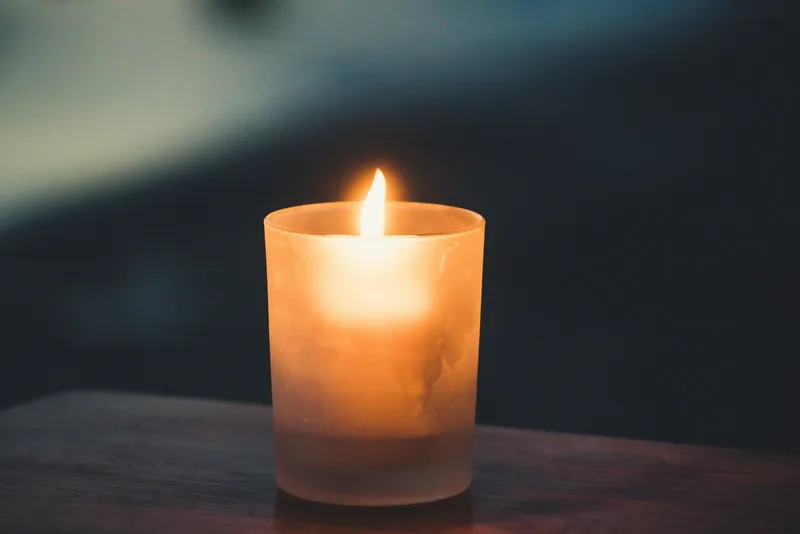 A single lit candle in a frosted glass on a dark wooden table