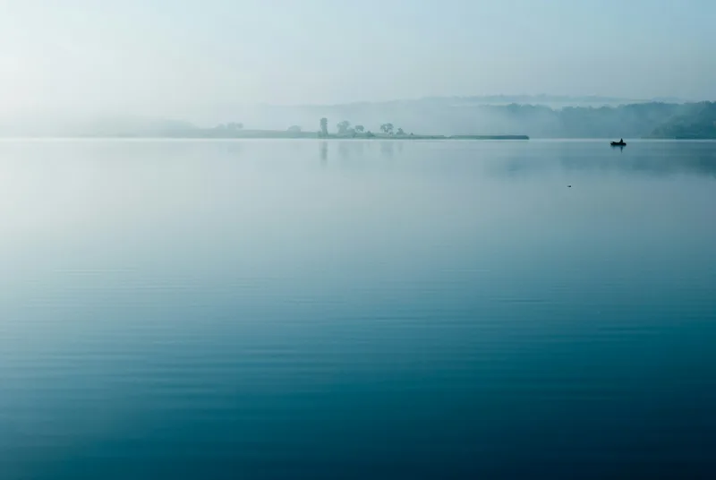 Mist rising over calm, still water at dawn