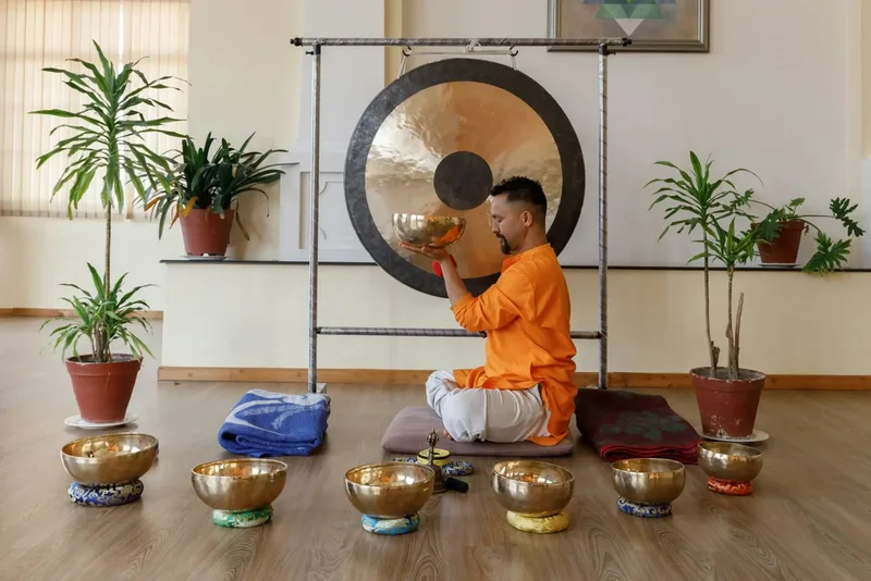 A facilitator plays singing bowls and a large gong during a sound bath session.