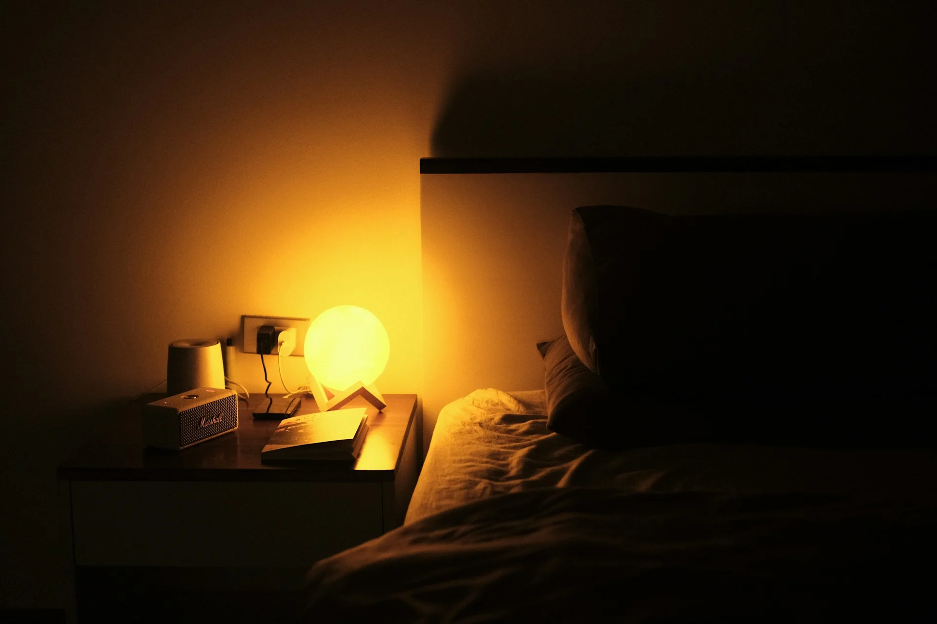 A softly lit bedroom at night with rumpled sheets and a warm bedside lamp