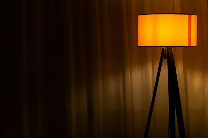 A warm floor lamp glowing beside a curtain in the evening