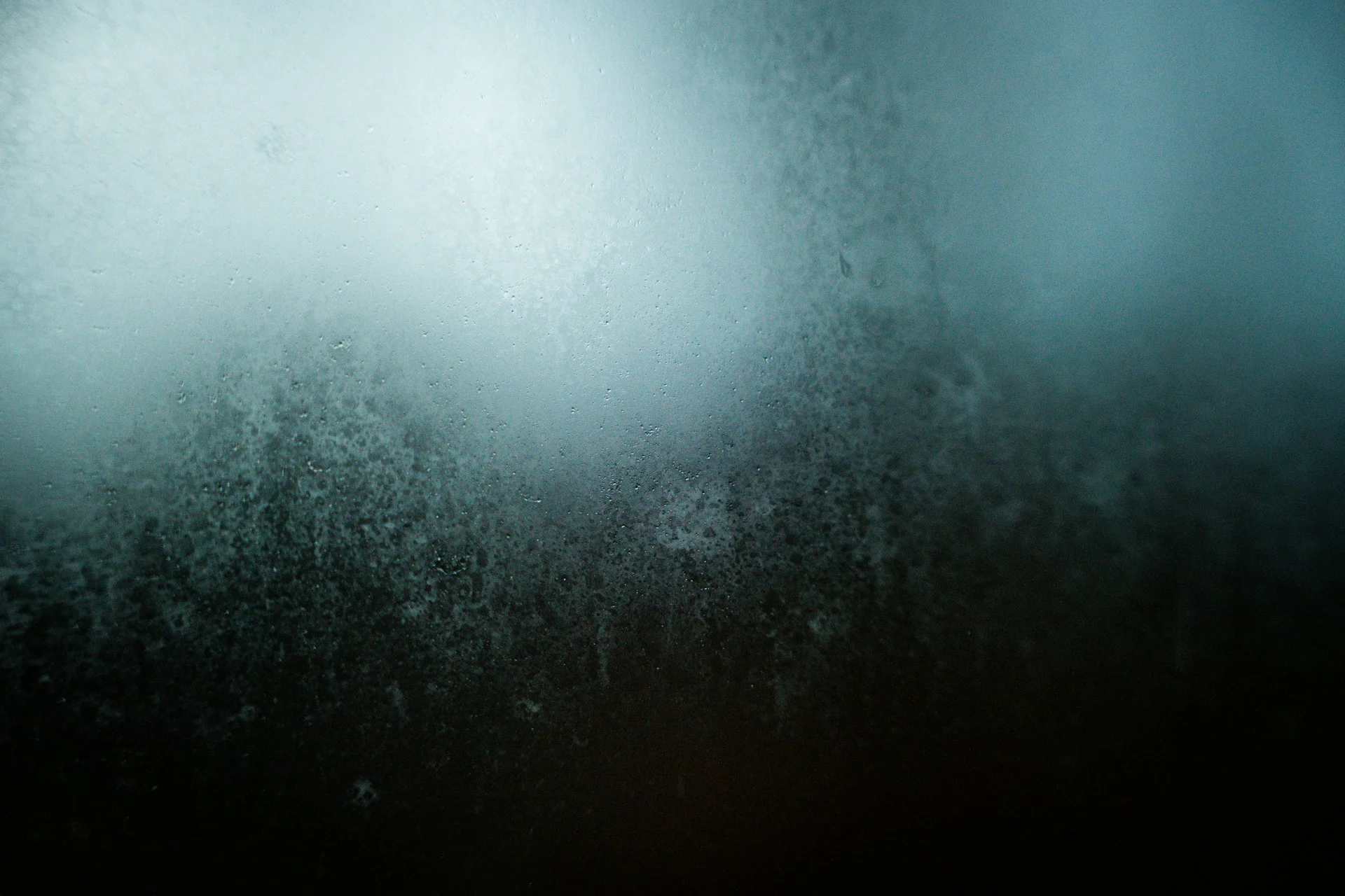 Soft light glowing through a misted, frosted window on a dark, calm morning