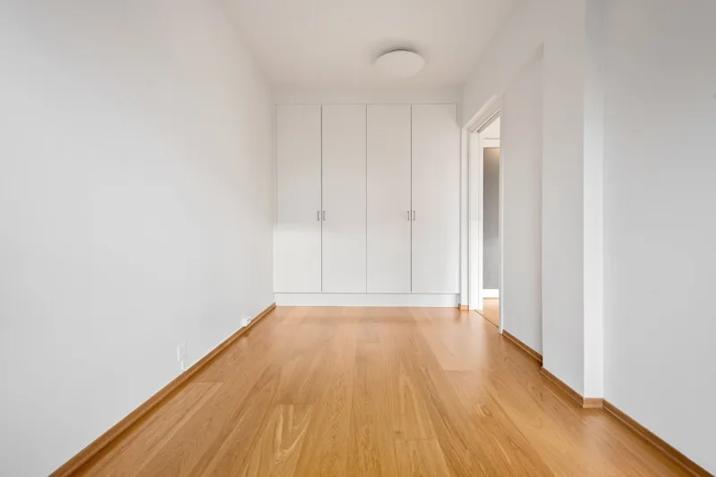 An empty room with a bare wood floor and white walls