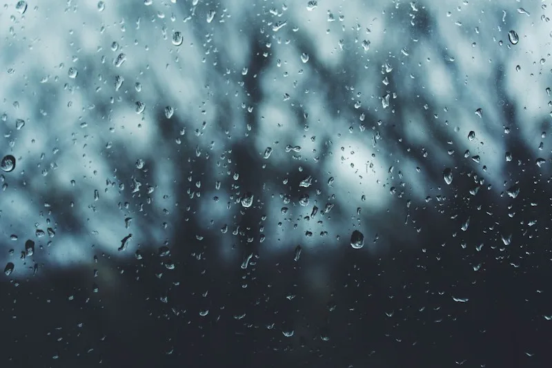 Soft water droplets on a window with a blurred view behind, evoking welling emotion