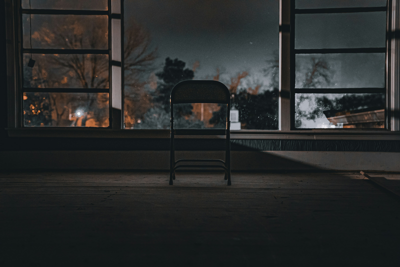 An empty armchair facing a window at night.