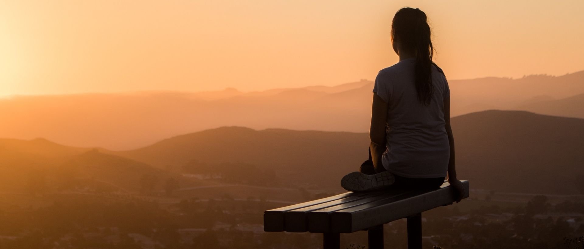 a woman sitting on a bench looking at the mountains.