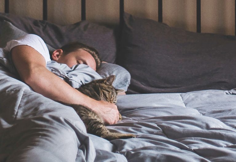 a man sleeping in bed with his cat.