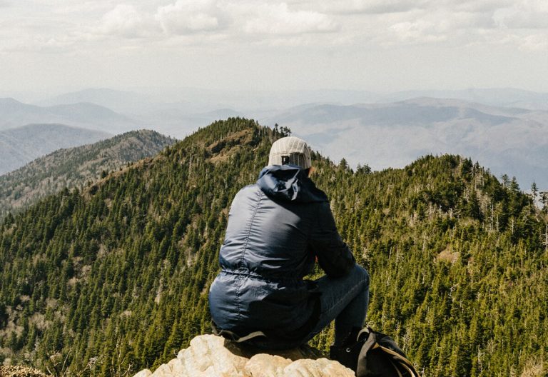 a man sitting on top of a mountain looking at the mountains.