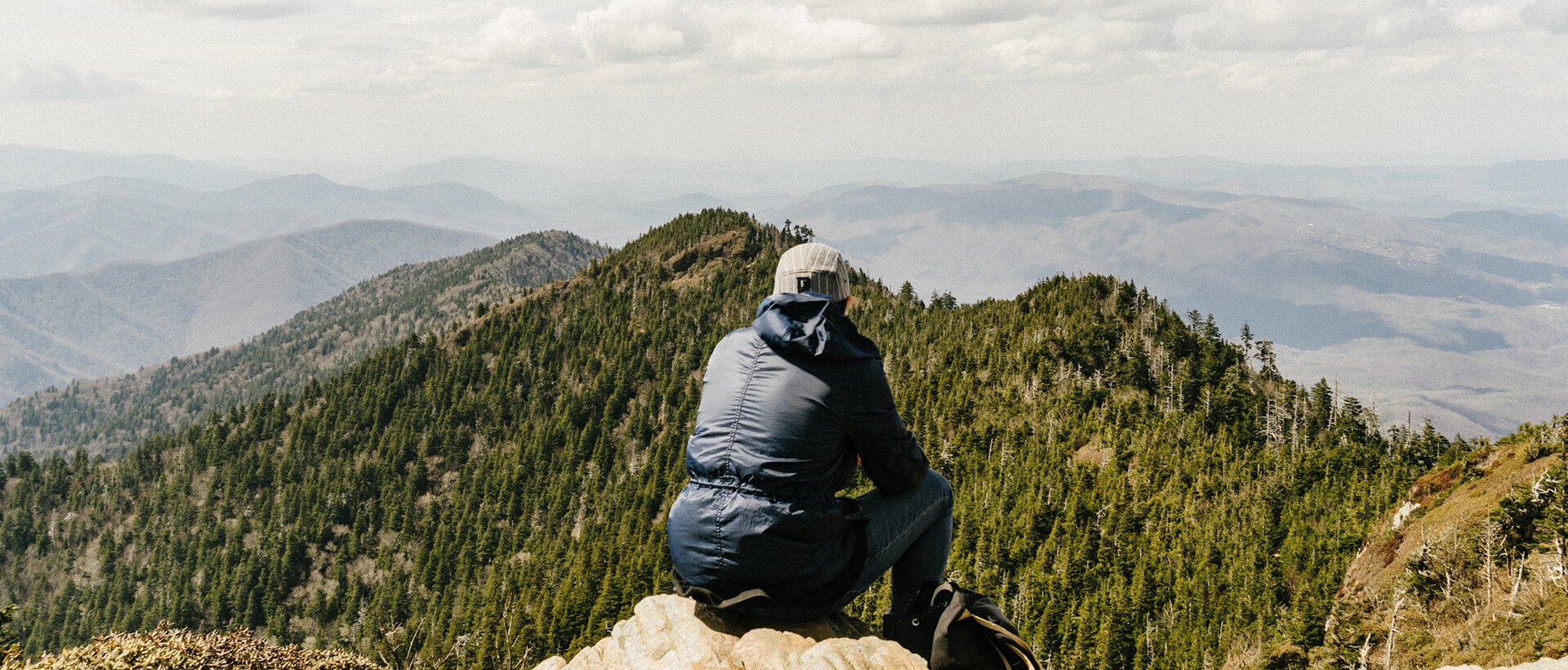 a man sitting on top of a mountain looking at the mountains.