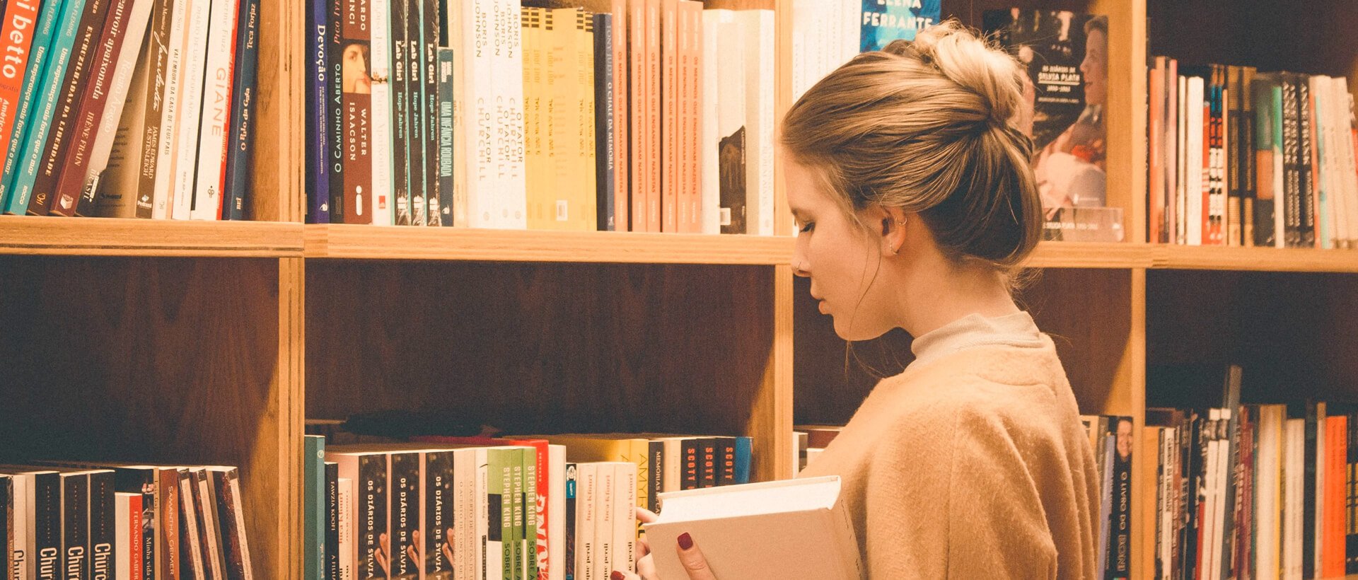 a woman reading a book in front of a bookshelf.
