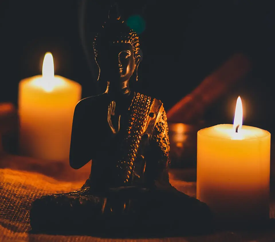 Buddha statue next to lit candles in the dark