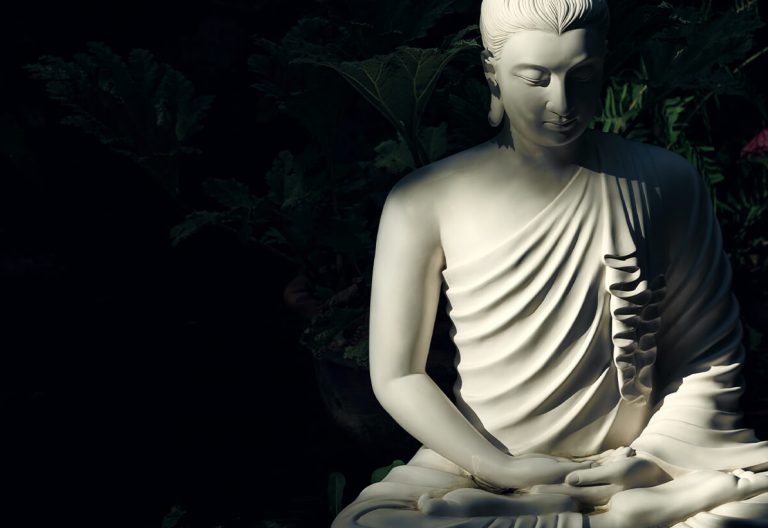 a white buddha statue sitting in the dark.