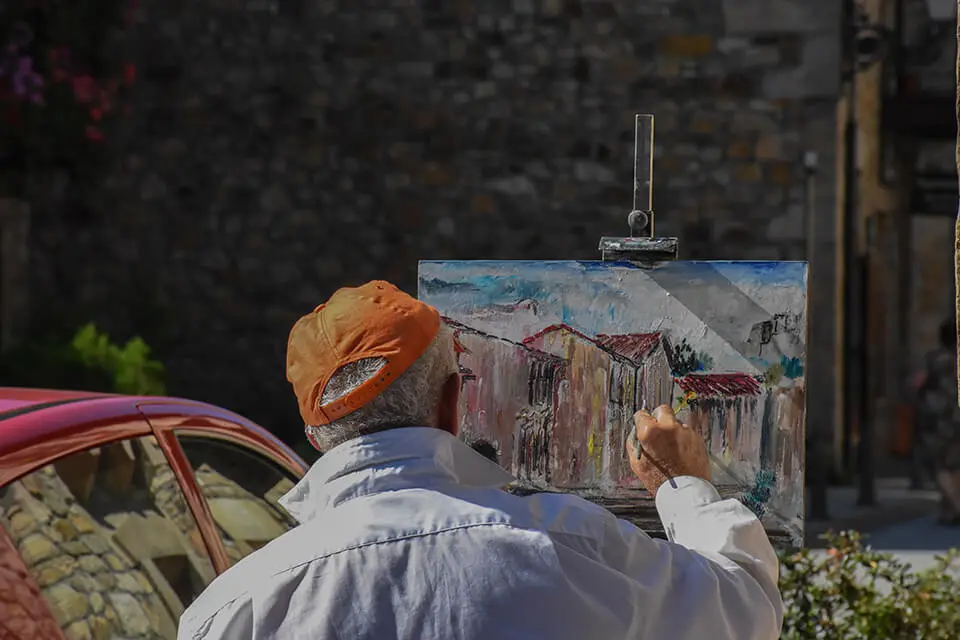 Older man painting on a canvas outside