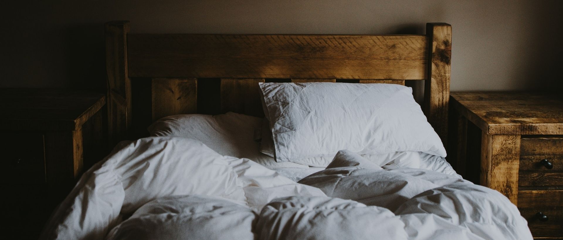an unmade bed with white sheets and pillows.