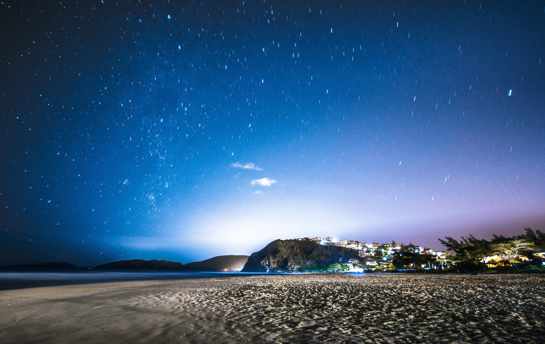 a night time view of a beach with a mountain in the background.