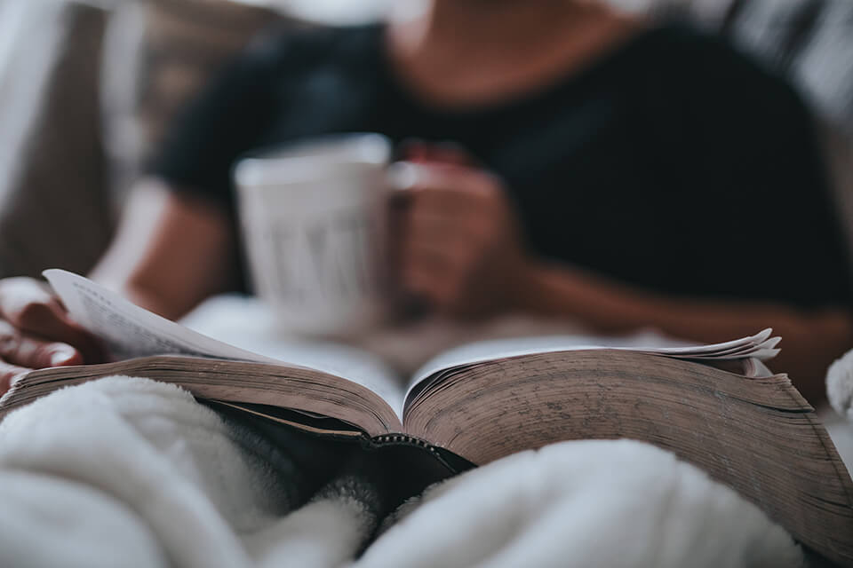 Man sitting in bed with coffee in hand, relaxing and reading
