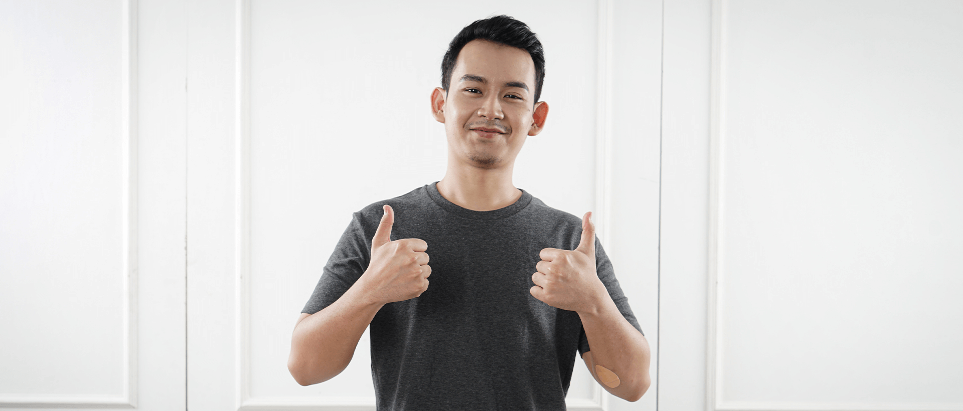 a man giving a thumbs up in front of a white wall.