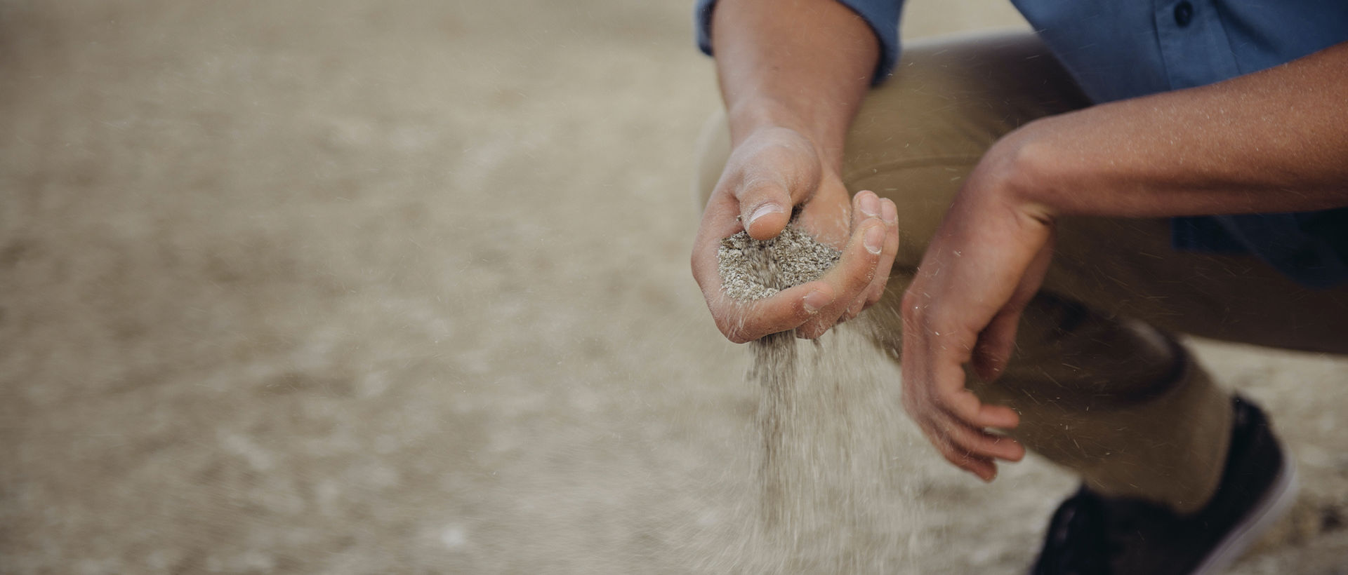 a man kneeling down holding a handful of sand.