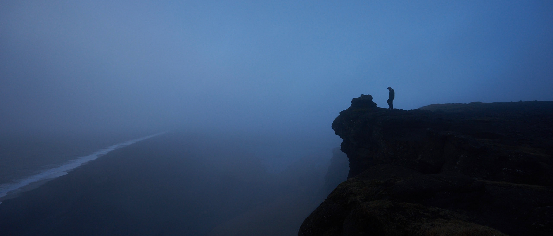 a person standing on top of a cliff on a foggy day.