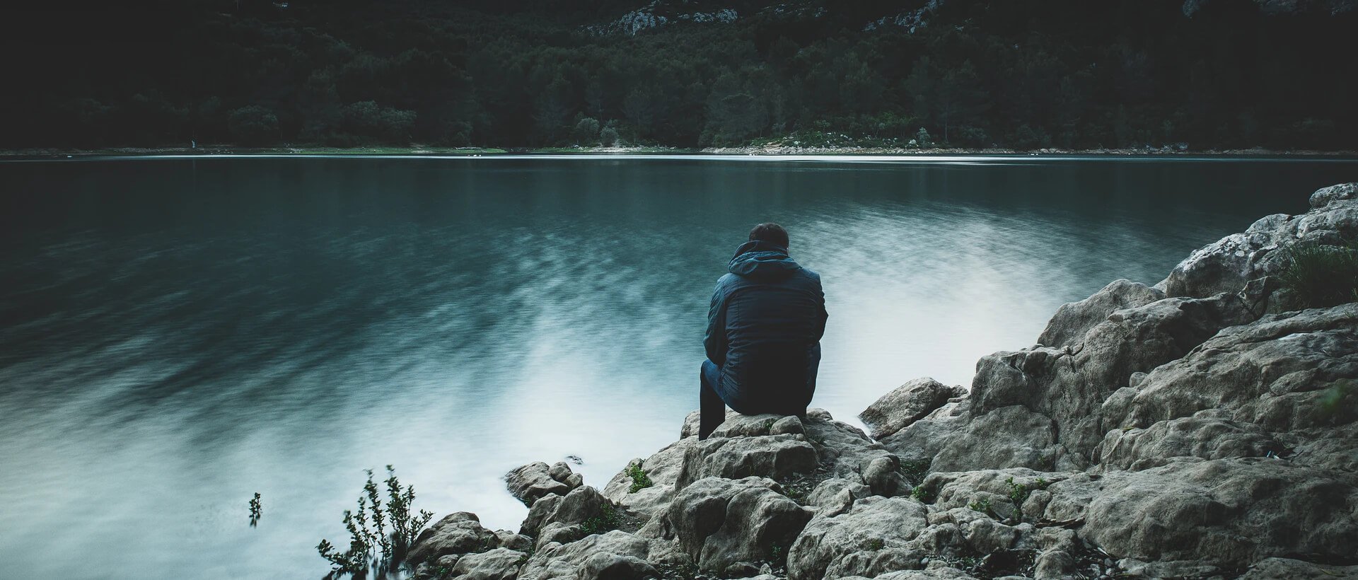a person sitting on top of a rock next to a body of water.