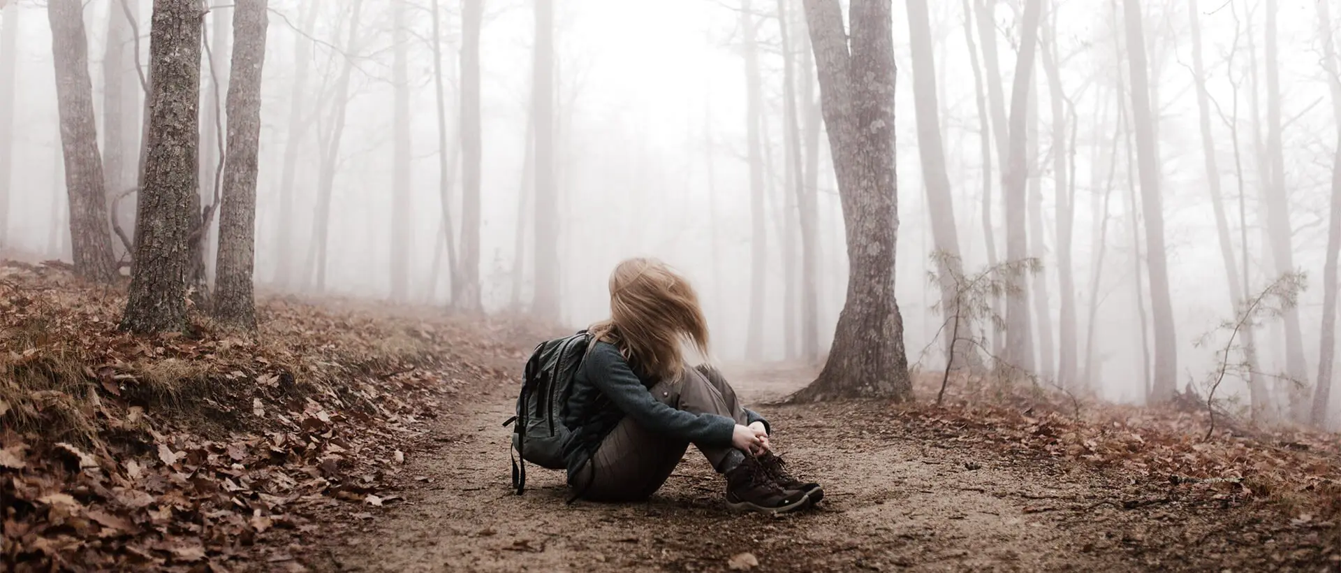 a woman sitting on a trail in a foggy forest.