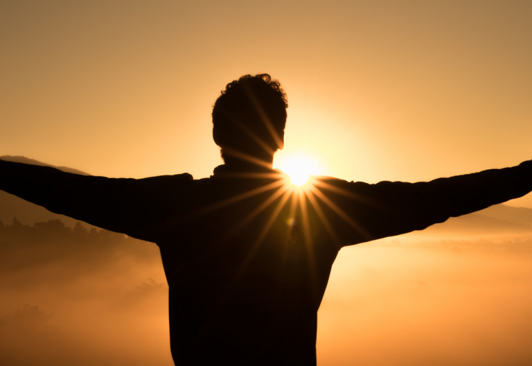 a man standing in front of the sun with his arms outstretched.