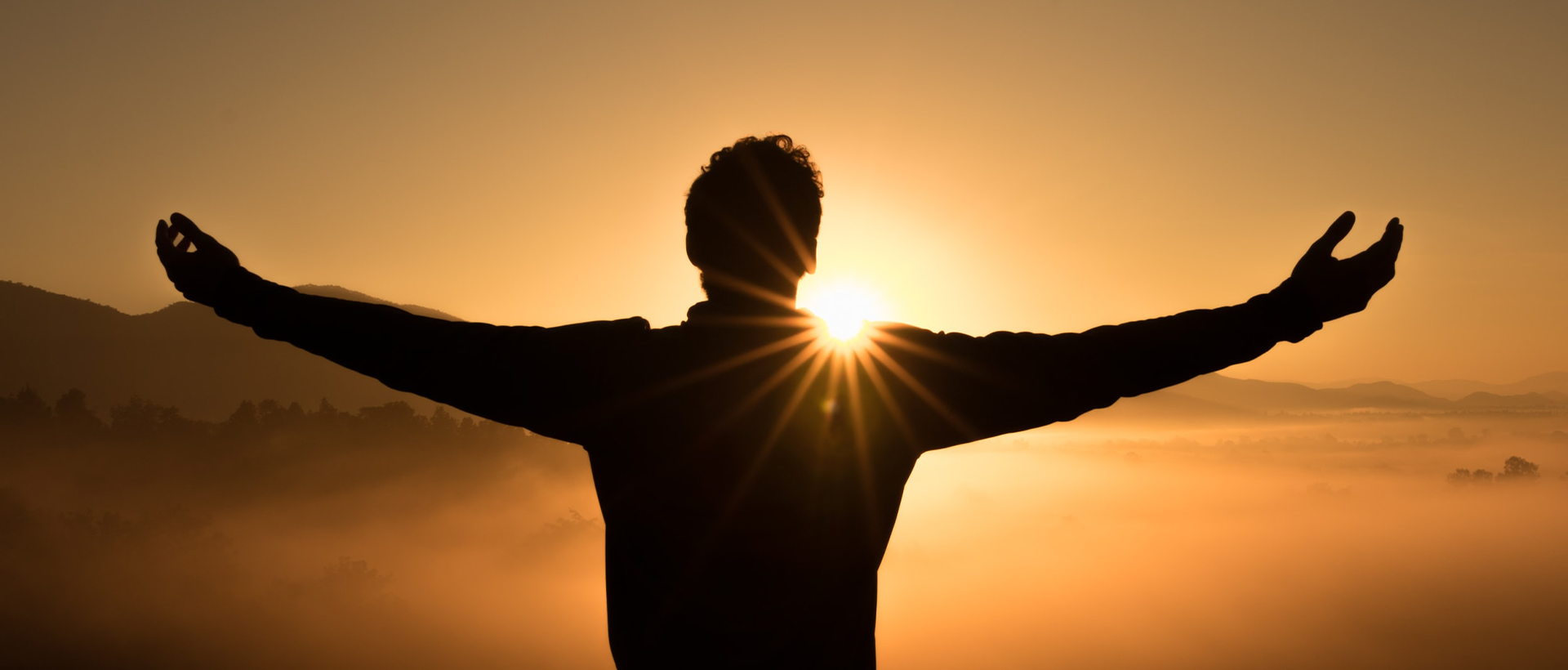 a man standing in front of the sun with his arms outstretched.