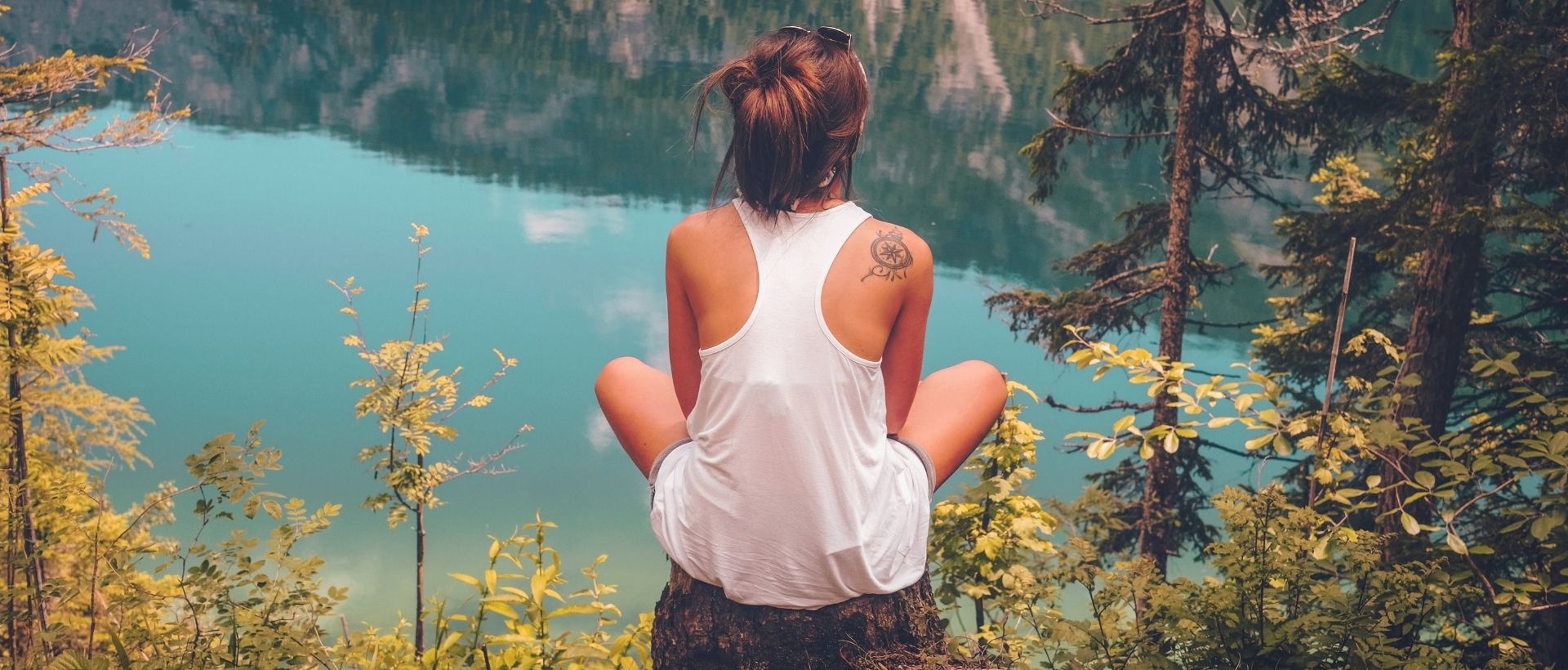a woman sitting on a rock looking out over a lake.