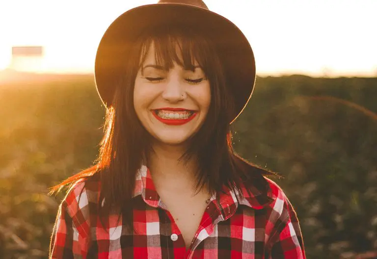 a woman in a plaid shirt and hat smiling.