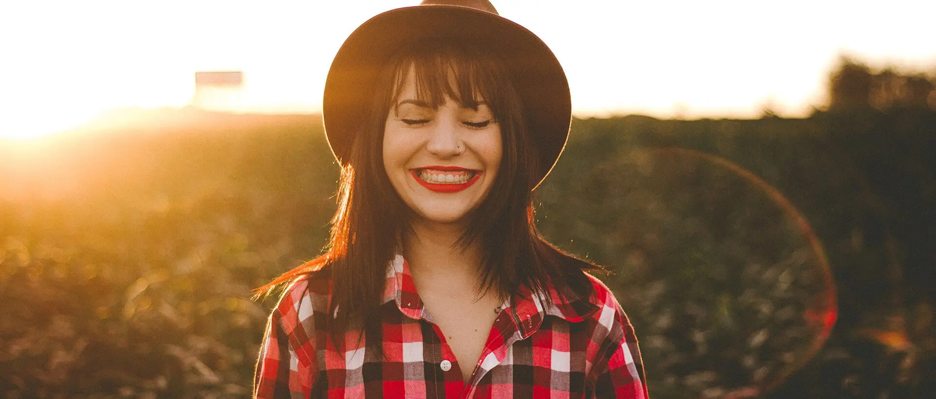a woman in a plaid shirt and hat smiling.